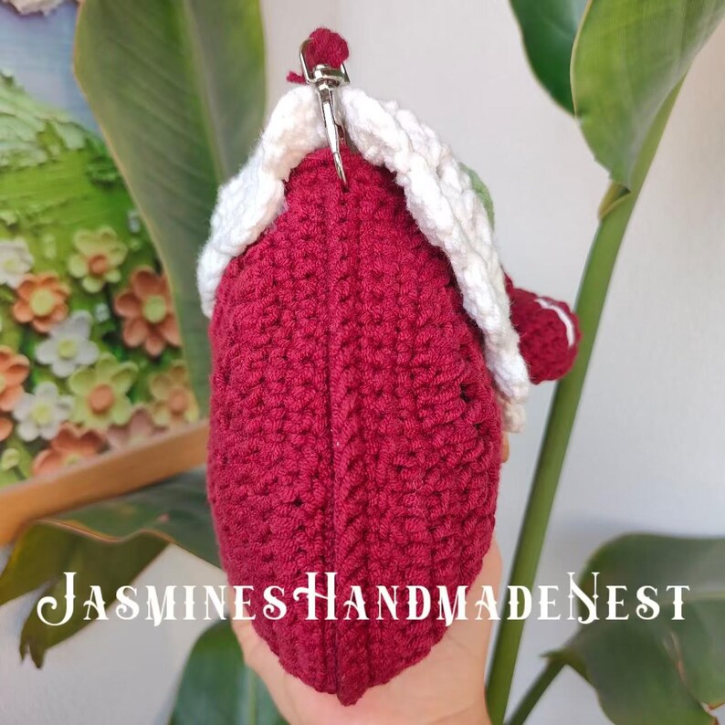 May include: A crocheted burgundy purse with a white crocheted trim and a silver clasp. The purse is held in a hand.