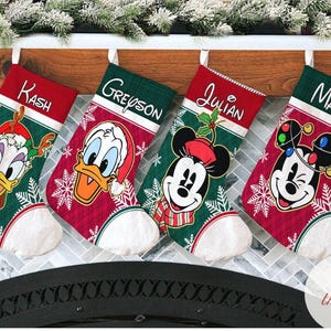May include: Four Christmas stockings with Disney characters: Donald Duck, Mickey Mouse, and Minnie Mouse. Each stocking has a name embroidered on the top. The stockings are red and green with white accents and snowflakes.