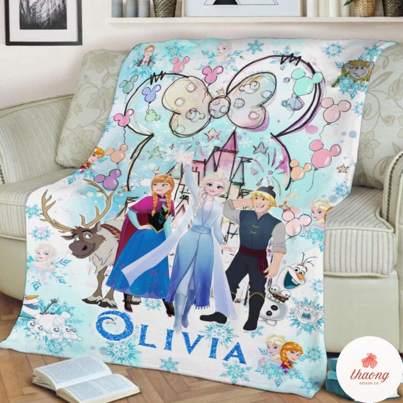May include: A light blue fleece blanket featuring characters from the movie Frozen, including Elsa, Anna, Kristoff, and Olaf. The blanket has a castle, snowflakes, and a large bow design. The name "OLIVIA" is printed on the blanket.
