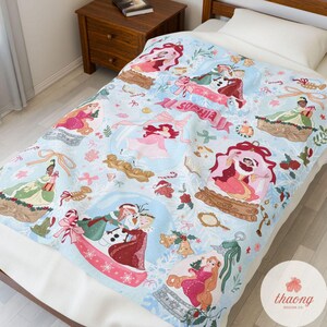 Puede incluir: Manta azul claro con ilustraciones de princesas de dibujos animados en bolas de nieve, con el nombre "Sophia" en una pancarta. La manta tiene un tema invernal con copos de nieve, lazos y bastones de caramelo.