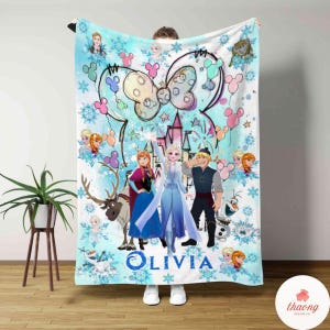 May include: A light blue blanket featuring characters from the movie Frozen, including Elsa, Anna, Kristoff, and Olaf. The blanket has a Minnie Mouse bow design and the name "Olivia" in blue script.