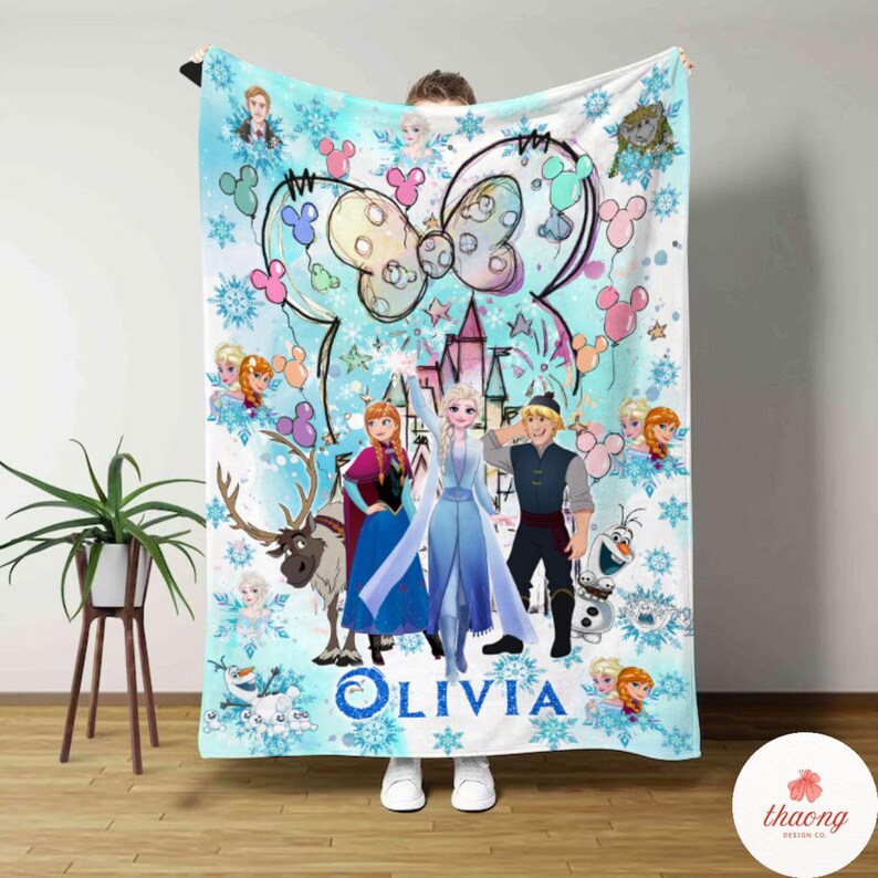 May include: A light blue blanket featuring characters from the movie Frozen, including Elsa, Anna, Kristoff, and Olaf. The blanket has a Minnie Mouse bow design and the name "Olivia" in blue script.