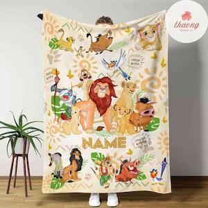 May include: A cream-colored blanket featuring illustrations of characters from The Lion King. The design includes Simba, Nala, Timon, Pumbaa, and other characters, with the words "NAME" and "Hakuna Matata" incorporated into the design.