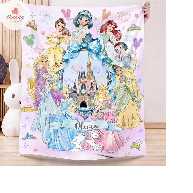 May include: A light purple fleece blanket featuring a central illustration of a castle surrounded by various animated princesses in colorful gowns. The design includes fireworks, stars, and balloons, with a blue ribbon banner displaying the name Olivia.
