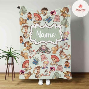 May include: A green and white personalized blanket featuring characters from the Toy Story movie franchise. The blanket has a large, green frame with the word "Name" in the center. The blanket is decorated with various Toy Story characters, including Woody, Buzz Lightyear, Jessie, and Mr. Potato Head.