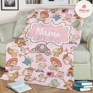 May include: Pink fleece blanket with a pink frame that says "Name" and a pattern of Toy Story characters, including Woody, Buzz Lightyear, Jessie, and Rex.