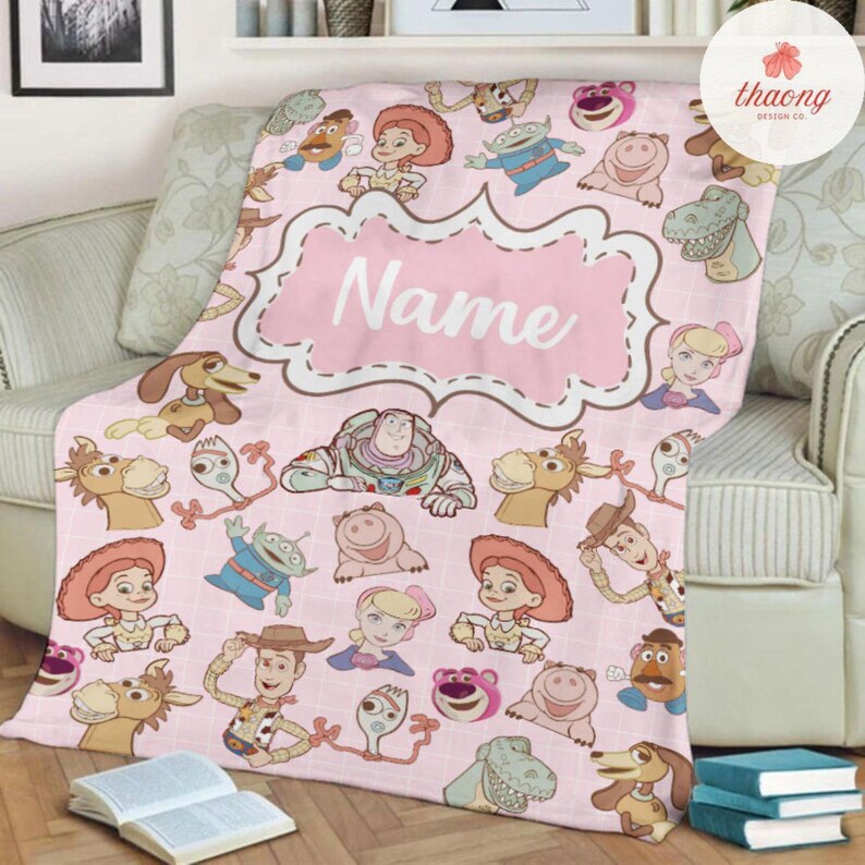 May include: Pink fleece blanket with a pink frame that says "Name" and a pattern of Toy Story characters, including Woody, Buzz Lightyear, Jessie, and Rex.