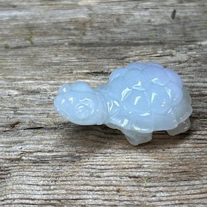 May include: A light blue, translucent turtle figurine. The turtle has a detailed shell pattern and is resting on a wooden surface. The figurine is a decorative item, possibly for a home or office.