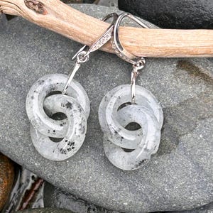 May include: A pair of silver earrings with a double-hoop design. The hoops are a marbled gray and white, with a speckled pattern. The earrings are hanging from a silver hook with small, clear stones.