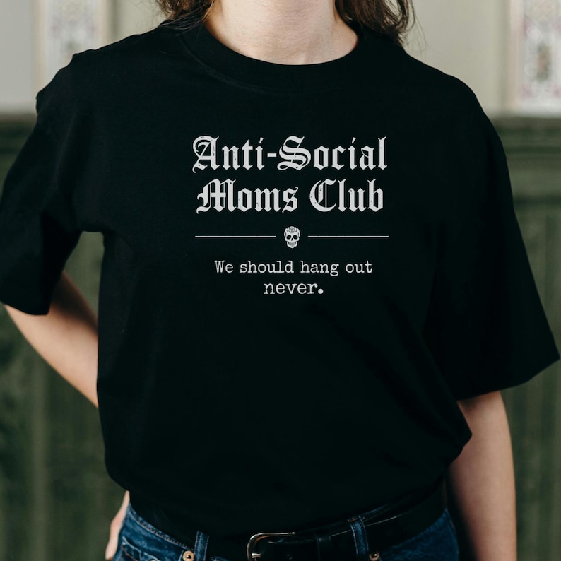 May include: Black t-shirt with the text "Anti-Social Moms Club" in a gothic font. Below the text is a skull graphic and the phrase "We should hang out never."