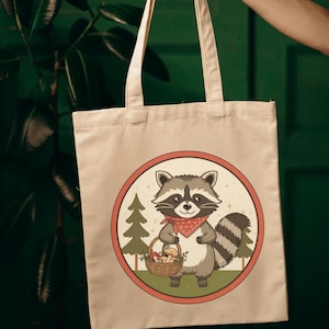 Può includere: Borsa tote beige con una grafica circolare di un procione con una bandana rossa e un cestino di funghi. Il procione è circondato da alberi e un bordo rosso e beige. La borsa ha un design semplice.