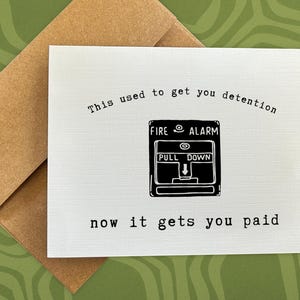May include: Greeting card with a brown envelope. The white card has a black illustration of a fire alarm and the text "This used to get you detention, now it gets you paid."