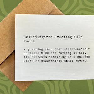 May include: A white greeting card with the text "Schrödinger's Greeting Card (noun)" and a definition of the term. The definition reads: "a greeting card that simultaneously contains $100 and nothing at all, its contents remaining in a quantum state of uncertainty until opened."