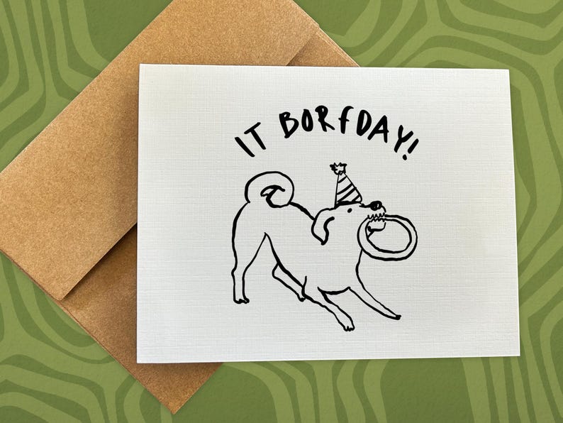 May include: A white greeting card with a black line drawing of a dog wearing a party hat and holding a ring in its mouth. The text "IT BORFDAY!" is above the dog. The card is paired with a brown envelope.