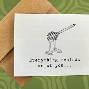 May include: A white card with a black and white illustration of a honey dipper dripping honey. The text on the card reads "Everything reminds me of you..."