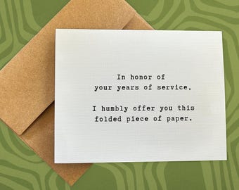 May include: A white card with the text "In honor of your years of service, I humbly offer you this folded piece of paper."