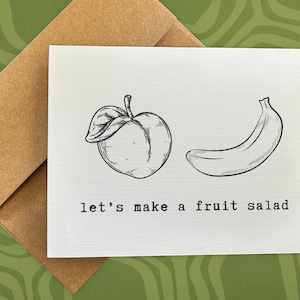 May include: A white card with a black and white illustration of a peach and a banana. The text "let's make a fruit salad" is printed below the illustration.
