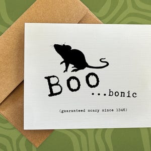 May include: A white greeting card with a black silhouette of a mouse above the word "BOO...bionic". The text "(guaranteed scary since 1346)" is printed below. The card is paired with a brown envelope.