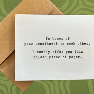 May include: A white card with the text "In honor of your commitment to each other, I humbly offer you this folded piece of paper."