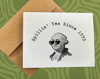 May include: A white greeting card with the text "Spillin' Tea Since 1773" and an image of George Washington wearing pixelated sunglasses. The card is paired with a brown envelope, set against a green patterned background.