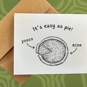 May include: A greeting card with a pie illustration and the phrase "It's easy as pie!" The pie is divided into two sections, labeled "yours" and "mine." The card is paired with a brown envelope, set against a green patterned background.