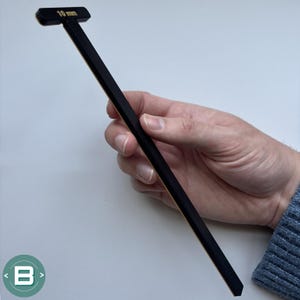 May include: A black and gold 10 mm T-shaped ruler with a pointed end.