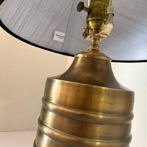 Op de afbeelding: Een messing tafellamp met een grijze lampenkap. De lampvoet heeft een spiraalvormig ontwerp. De lampenkap heeft een zwarte rand. De lamp heeft een vintage uitstraling.