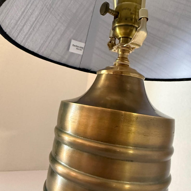 Op de afbeelding: Een messing tafellamp met een grijze lampenkap. De lampvoet heeft een spiraalvormig ontwerp. De lampenkap heeft een zwarte rand. De lamp heeft een vintage uitstraling.