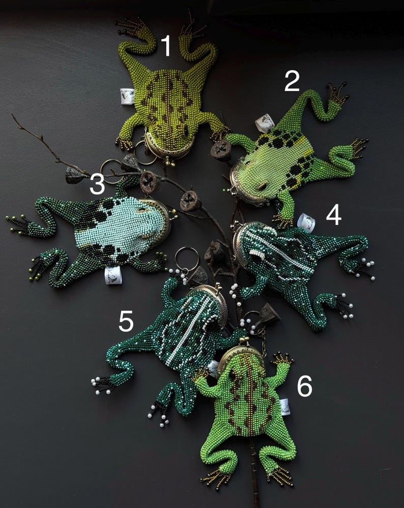 May include: A collection of six beaded frog-shaped coin purses in various shades of green, blue, and white. Each purse features a metal clasp and detailed beadwork, showcasing a unique design. The purses are arranged on a dark surface.