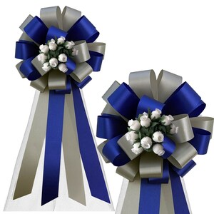 May include: Two blue and silver wedding chair sashes with white rosebuds. The sashes are tied in a bow with long tails.