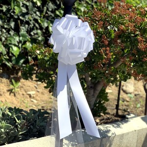 Large white bow with tulle tails displayed on a pole.