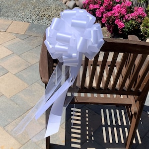 Large white pew bows with tulle tails on the back of a chair.