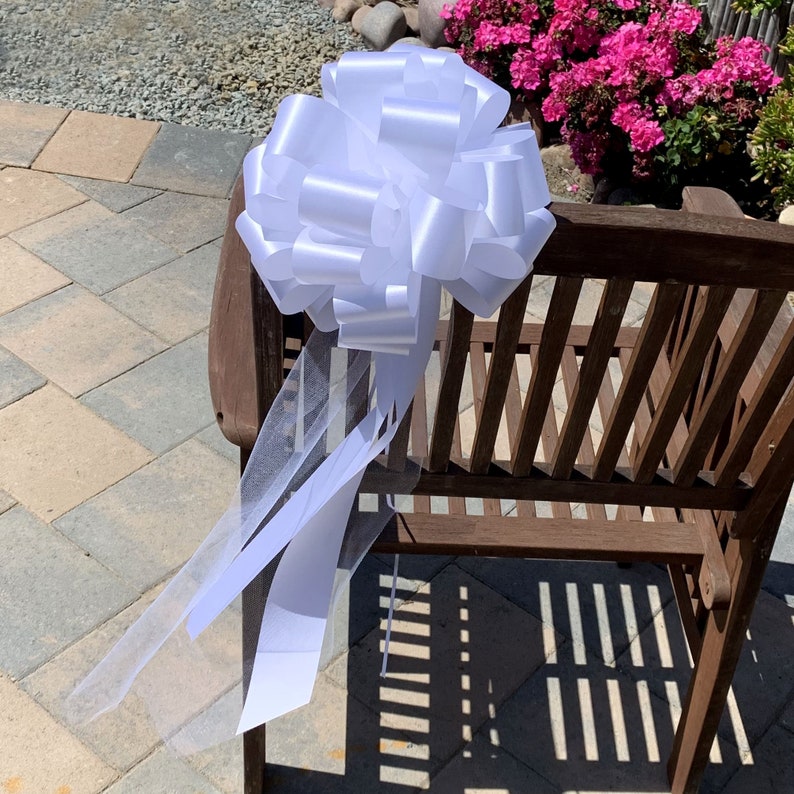 Large white pew bows with tulle tails on the back of a chair.