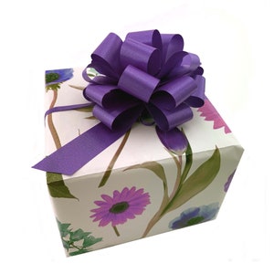 May include: A white gift box with a purple floral design and a large purple satin bow on top.