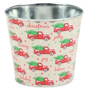 May include: A metal planter with a cream background and a repeating pattern of red pickup trucks carrying Christmas trees. The trucks have white snow on the roof and the words "peace", "christmas", "jolly", "merry", "joy", "noel", "believe", and "holiday" are printed on the planter.