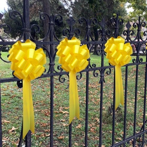 May include: Four yellow bows tied to a black metal fence. The bows are made of shiny, crinkled ribbon.