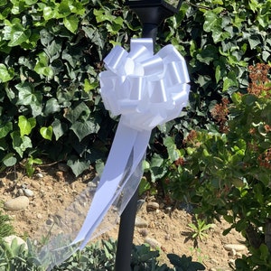 Large white bow with tulle tails displayed on a pole.