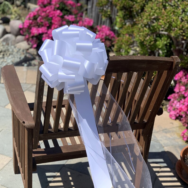 Large white bow with tulle tails displayed on the back of a chair.