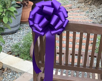 May include: A large purple satin bow tied with a long tail, attached to a wooden chair.