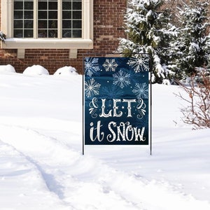 May include: A blue and white winter-themed garden flag with the text "& LET it SNOW" and snowflakes. The flag is displayed on a black metal stand in a snowy yard.