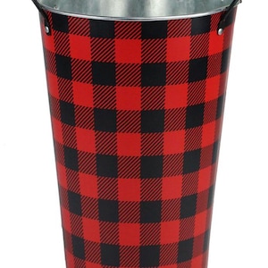 May include: A tall, cylindrical metal bucket with a red and black buffalo plaid pattern. The bucket has a silver interior and black handles. This decorative bucket is suitable for various uses.