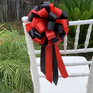 May include: A red and black bow tied to a white chair. The bow is made of satin ribbon and is tied in a large, elaborate knot.