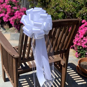 Large white bow with tulle tails displayed on the back of a chair.