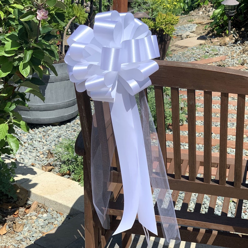 Large white bow with tulle tails displayed on the back of a chair.