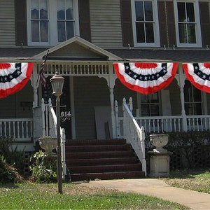 3 bunting flags hanging from the porch of a 2 story home.