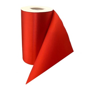 May include: A roll of bright red satin ribbon. The ribbon is rolled up on a white cardboard core and is partially unrolled, showing the smooth, shiny surface of the ribbon.