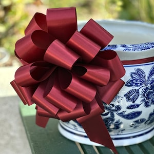 May include: A large, burgundy satin bow with a long tail. The bow is tied around a white ceramic planter with a blue and white floral pattern.