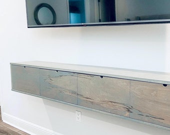 May include: A long, light gray wooden media console with four drawers. The console is mounted to the wall and has a modern, minimalist design.
