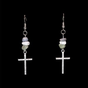 May include: A pair of dangle earrings with a silver cross pendant. The earrings feature a series of small, colorful stones in shades of blue, white, and green. The cross is encrusted with small, clear stones.