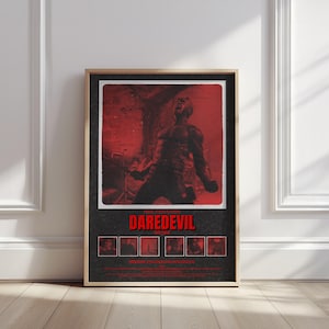 May include: Framed poster featuring a red and black image of Daredevil. The poster has a distressed look, with the title "DAREDEVIL" in bold red letters. The image shows a figure in a fighting stance. The poster is in a wooden frame.